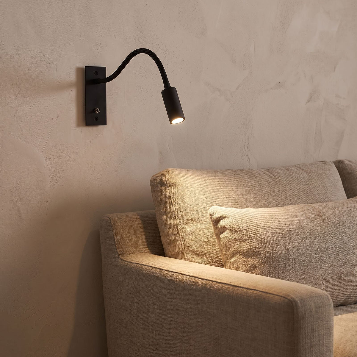 Flexible gooseneck reading wall light beside a living room sofa at night