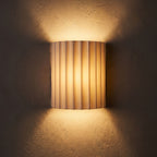 Fluted Resin Wall Light glowing on a plaster wall at night