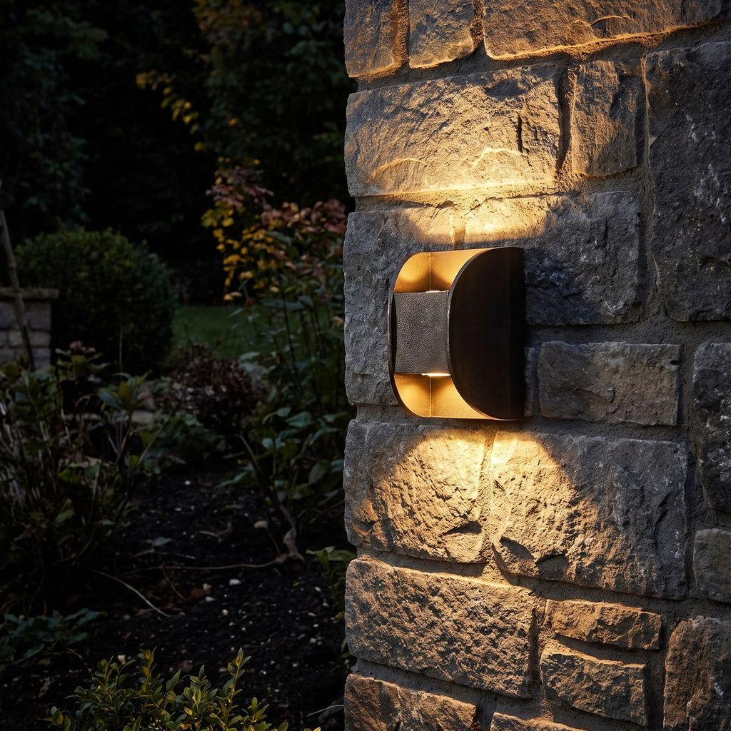 Forged Metal Mini Up Down Outdoor Wall Light glowing on a garden wall at night