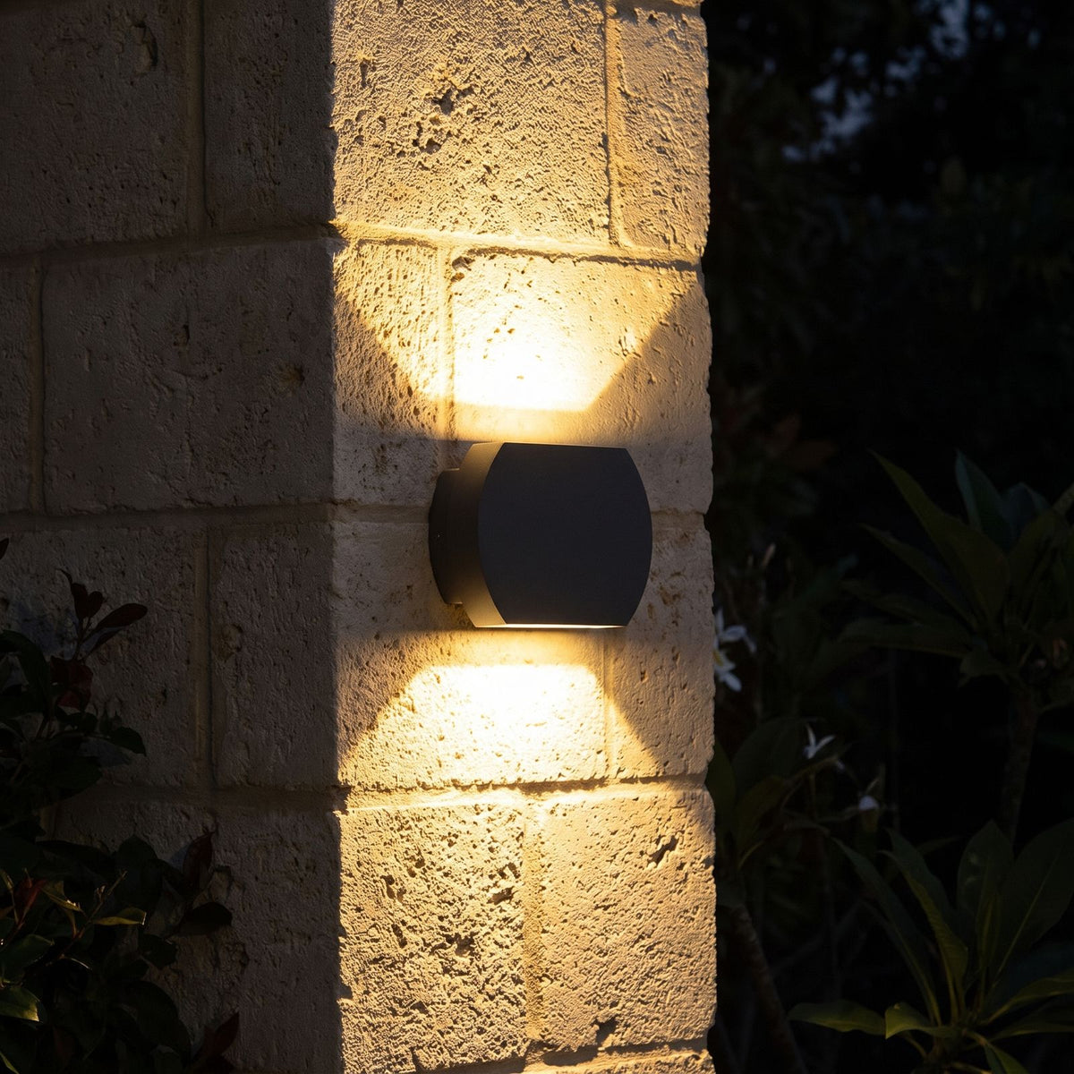 Geometric Glass Up Down Outdoor Wall Light glowing on a garden wall at night
