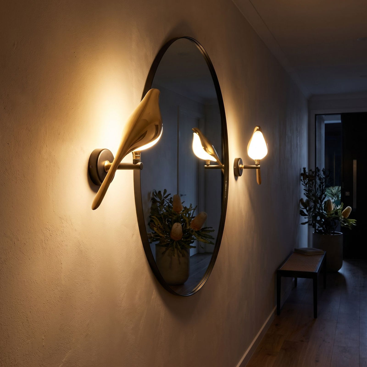 Gold bird sculpture LED wall light beside a round mirror in an entry hall at night