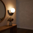 Half moon iron and opal globe wall light beside a round mirror in an entry hall at night