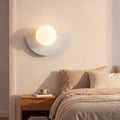 Half Moon Iron and Opal Globe Wall Light in white beside a bed