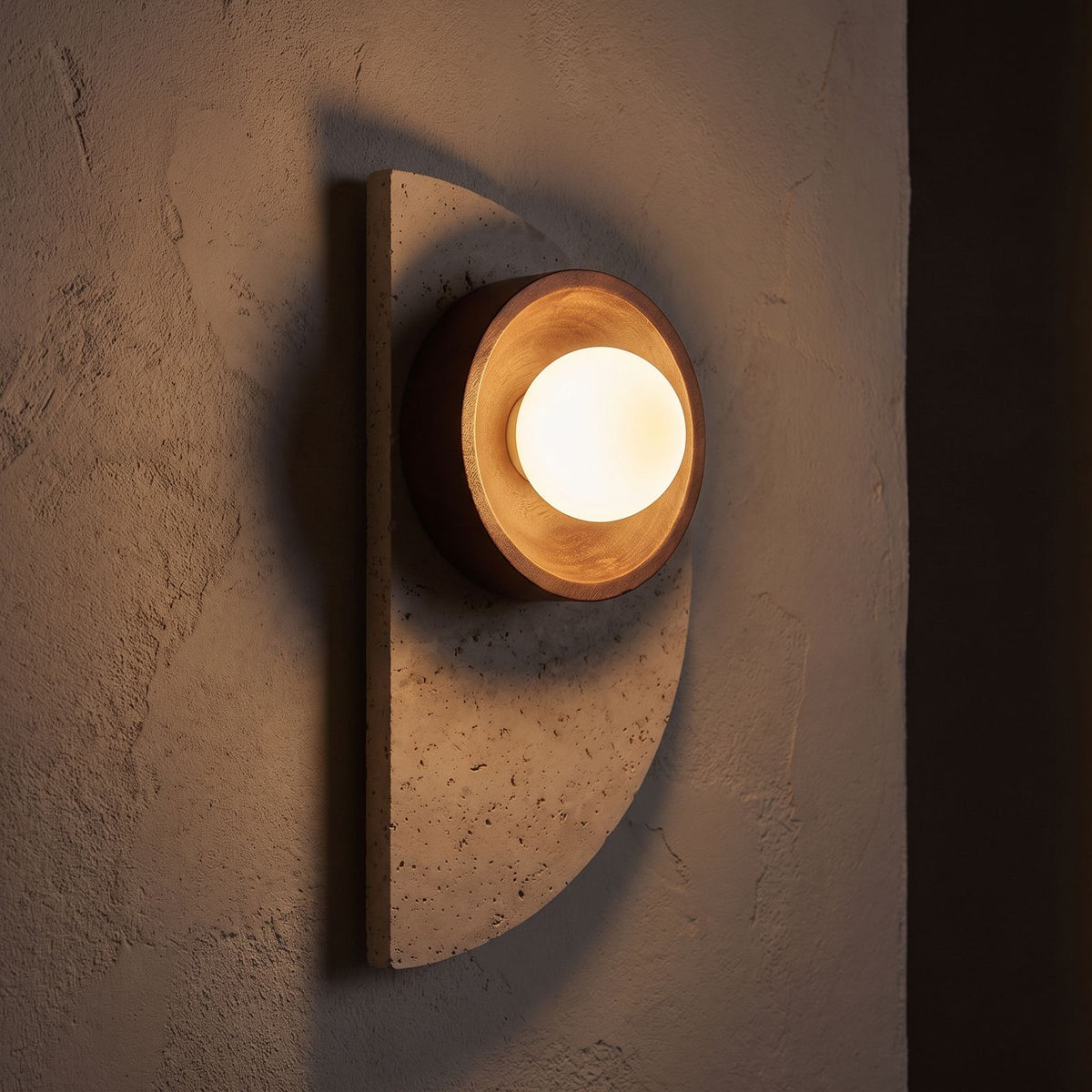 Half Moon Travertine and Wood Wall Light glowing on a plaster wall at night