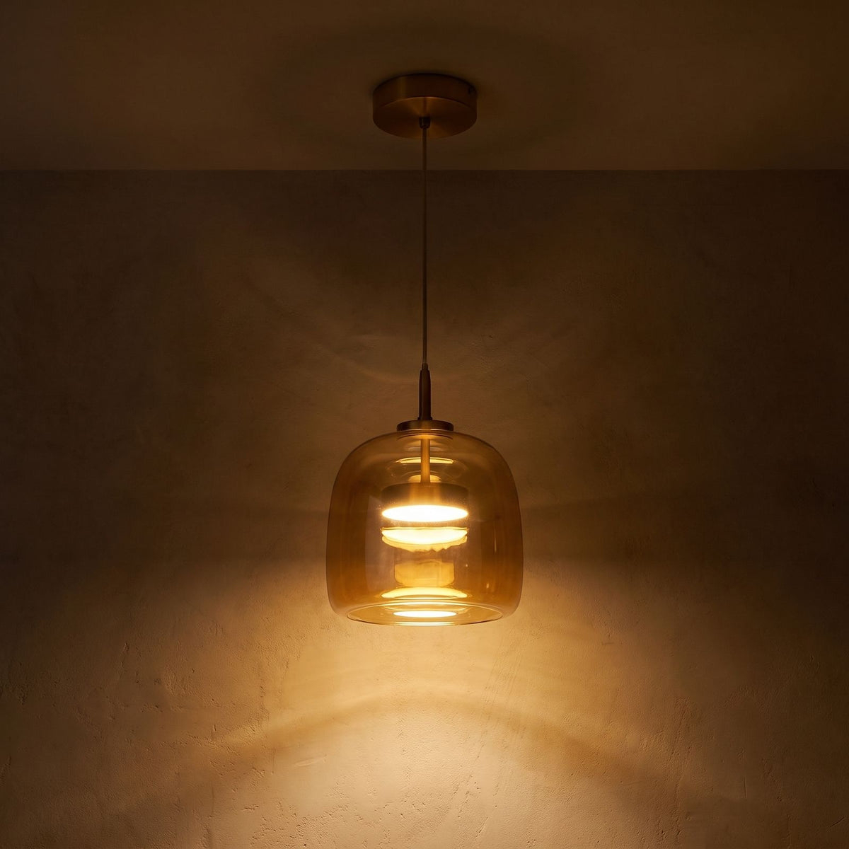 Hand Blown Glass LED Pendant Light glowing against a plaster wall at night