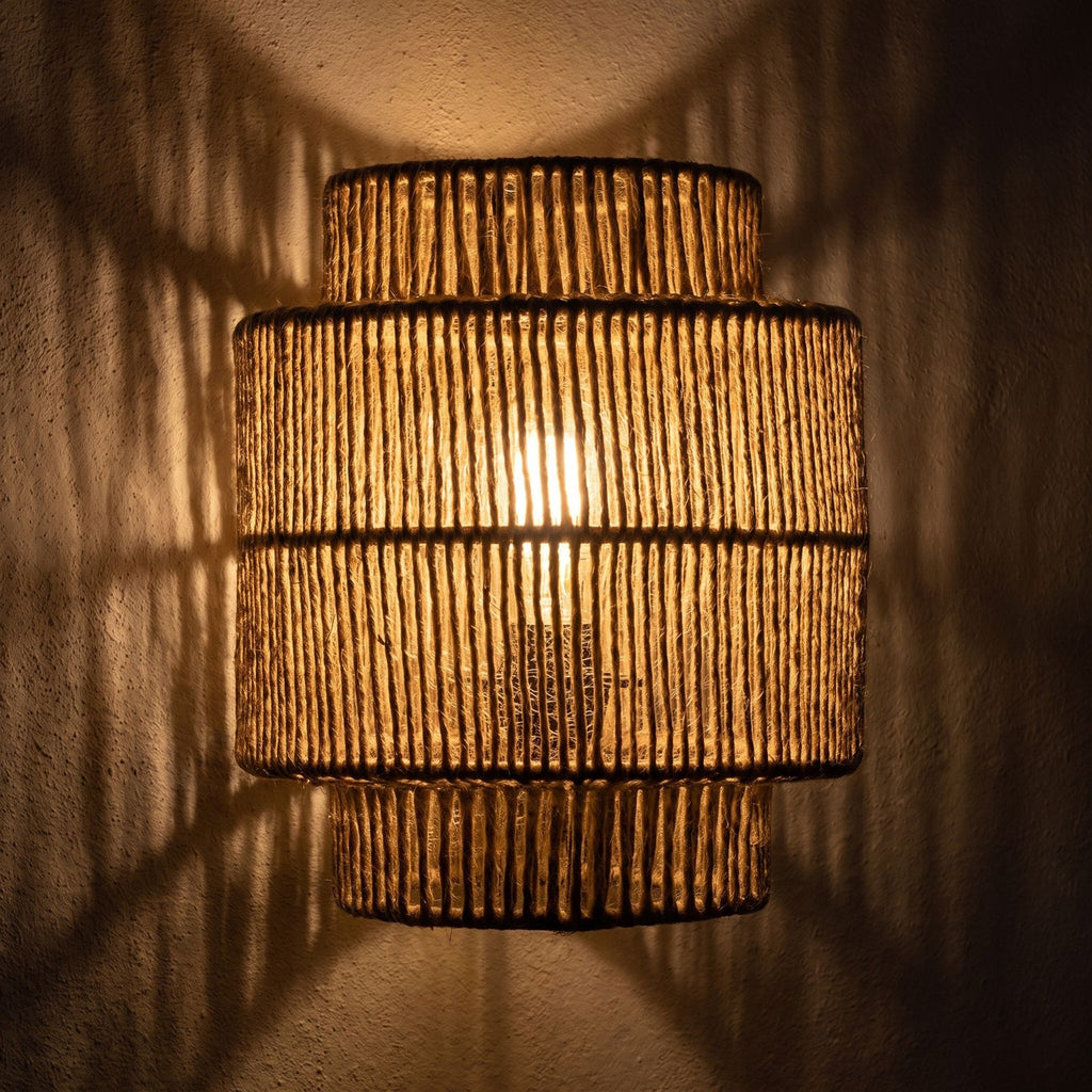 Hand Woven Natural Fibre Up Down Wall Light glowing on a plaster wall at night
