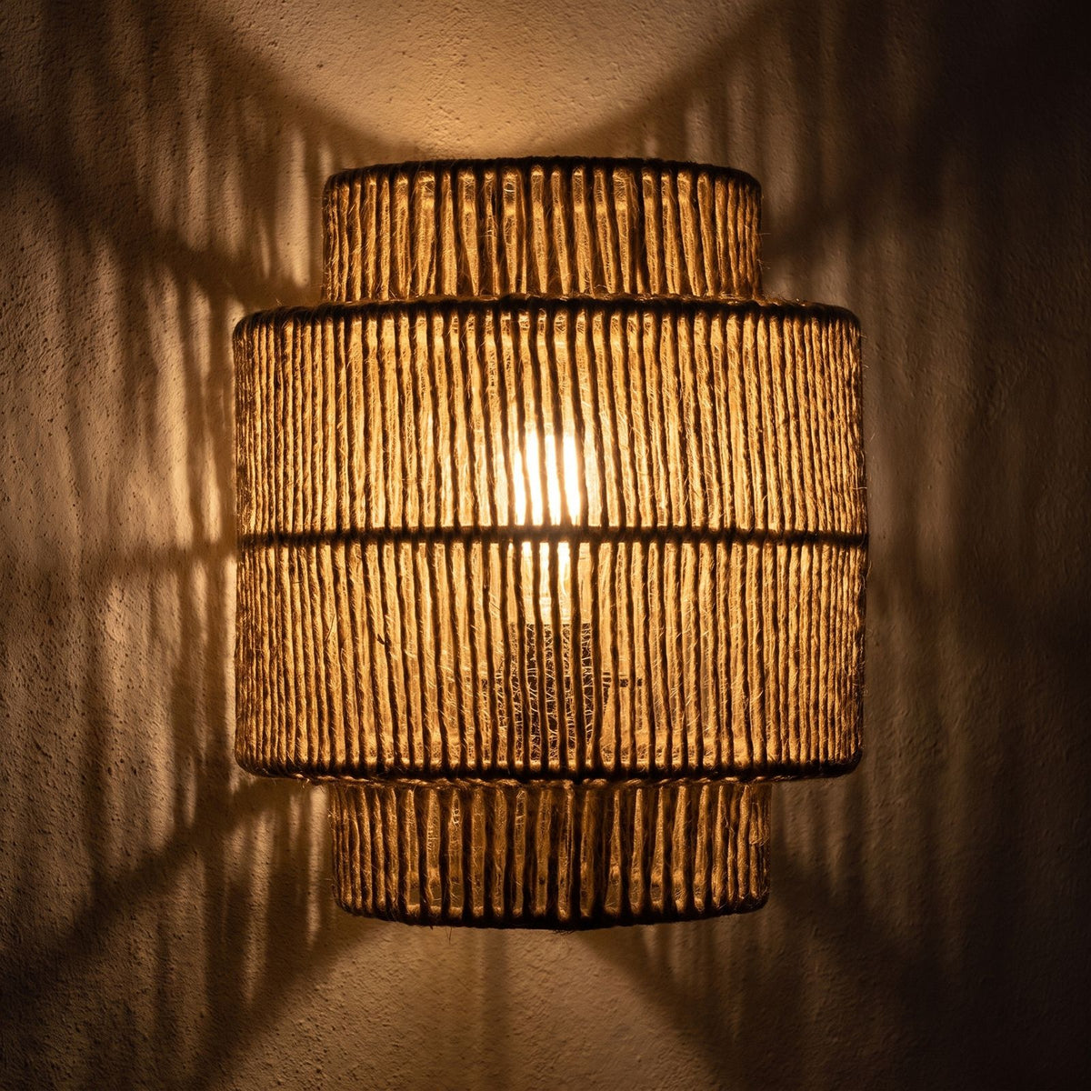 Hand Woven Natural Fibre Up Down Wall Light glowing on a plaster wall at night