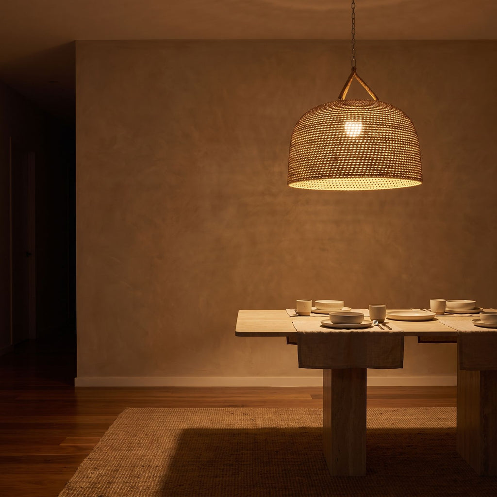 Handwoven Rattan Japandi Pendant Light glowing against a plaster wall at night