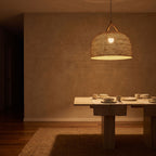 Handwoven Rattan Japandi Pendant Light glowing against a plaster wall at night