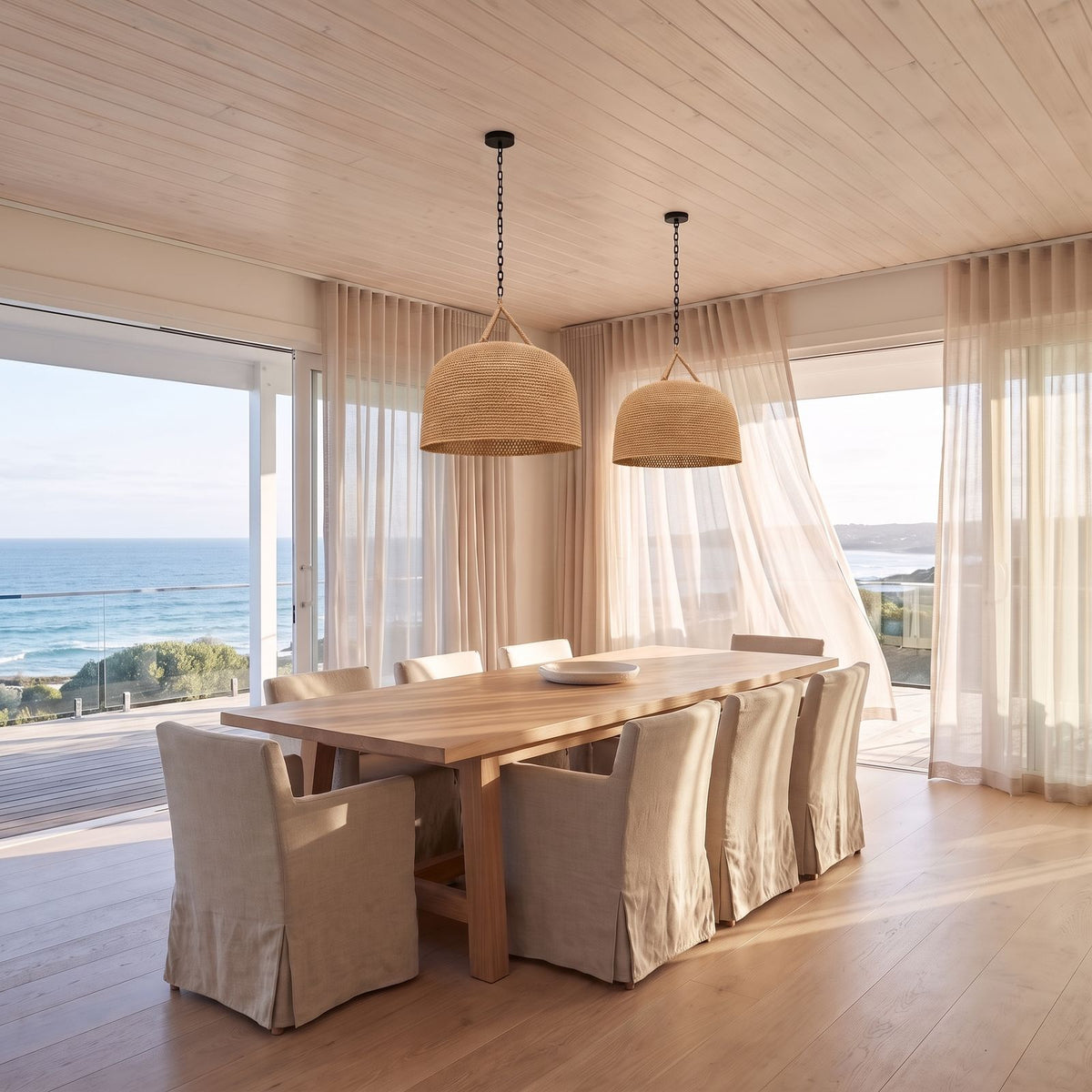 A pair of Handwoven Rattan Japandi Pendant Lights, Ø45 cm, over a dining table in a beach house with ocean view