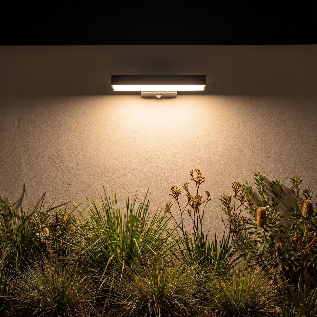 Horizontal flat bar outdoor wall light on a garden wall at night