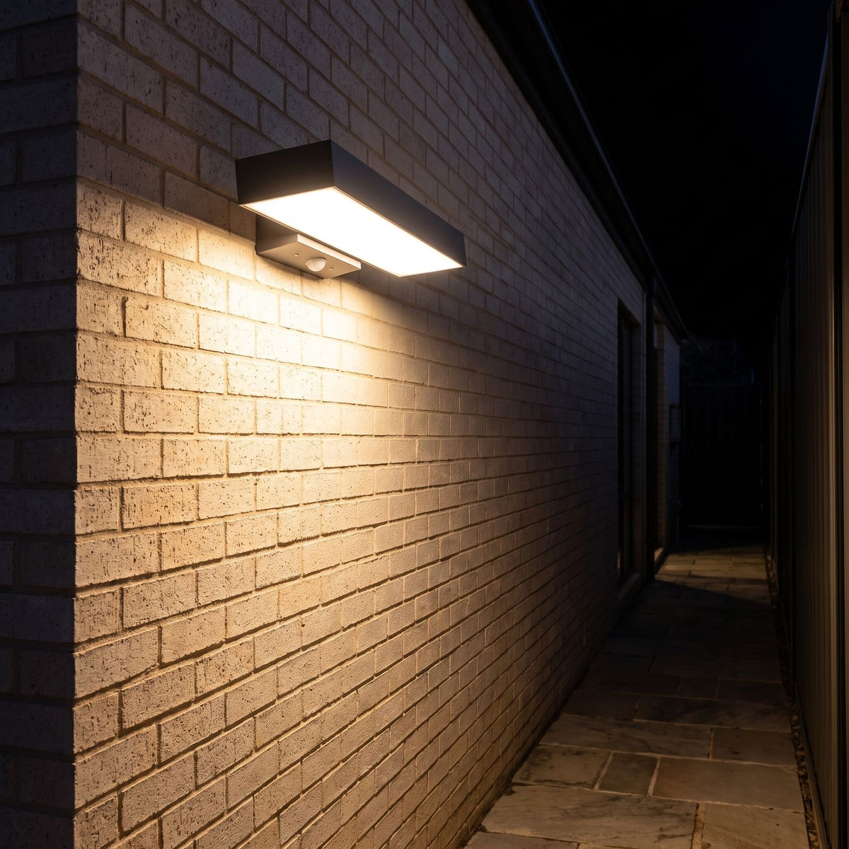 Horizontal flat bar outdoor wall light along a side passage at night