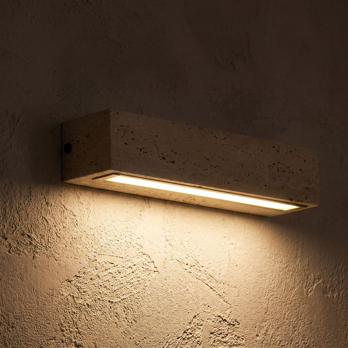 Horizontal Yellow Travertine Bar Wall Light glowing on a plaster wall at night