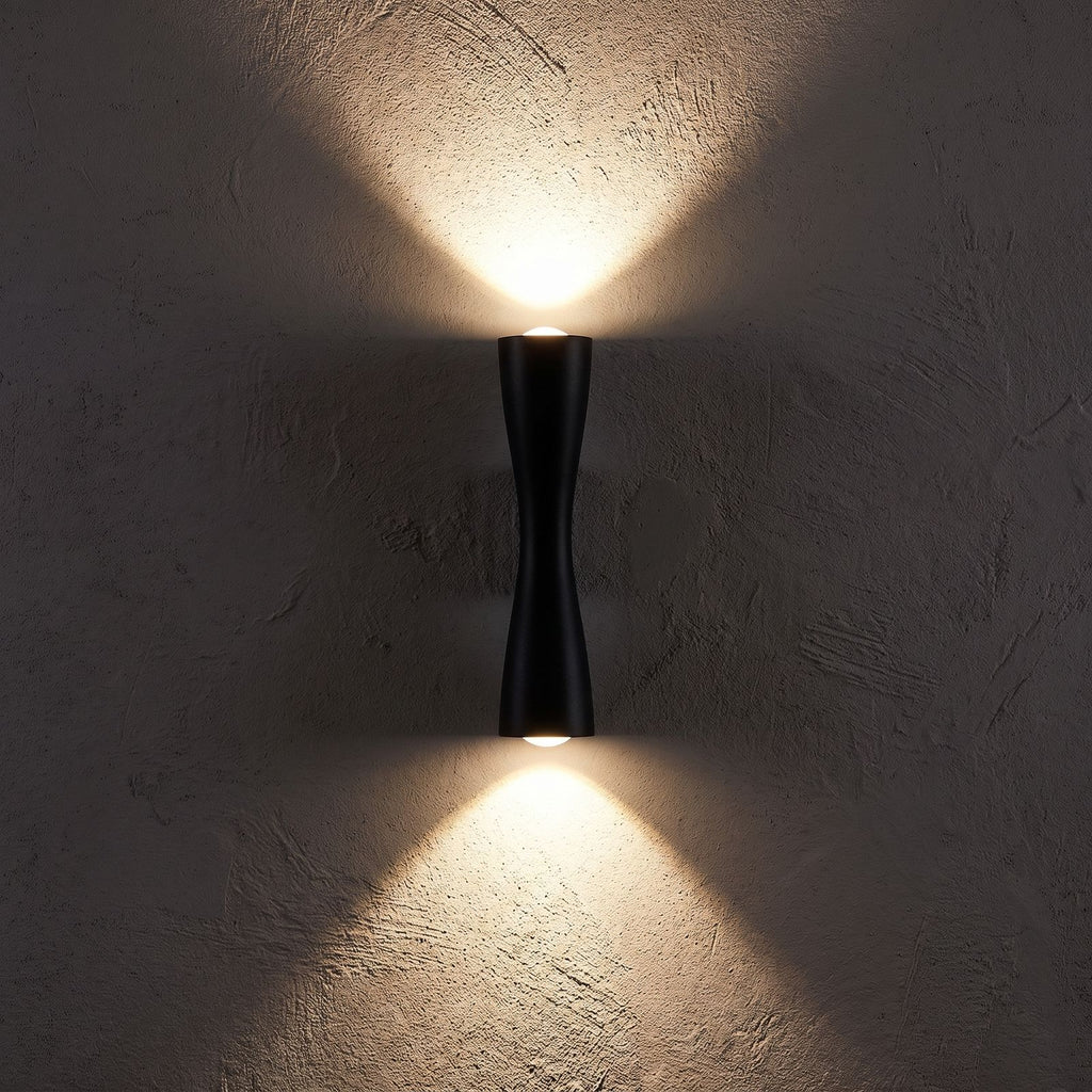 Hourglass Aluminium Up Down Wall Light glowing on a plaster wall at night