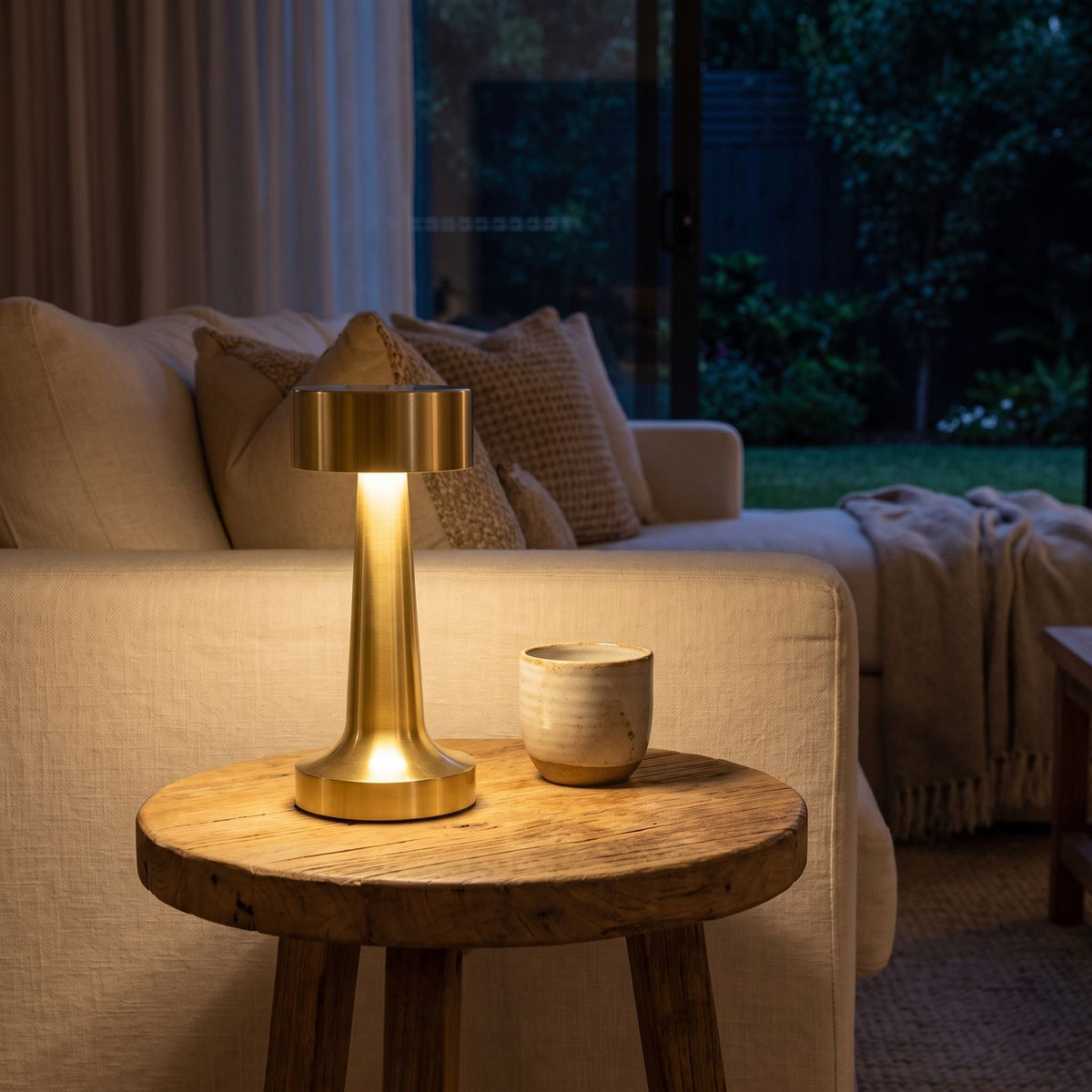 Gold hourglass rechargeable table lamp on a side table beside a sofa
