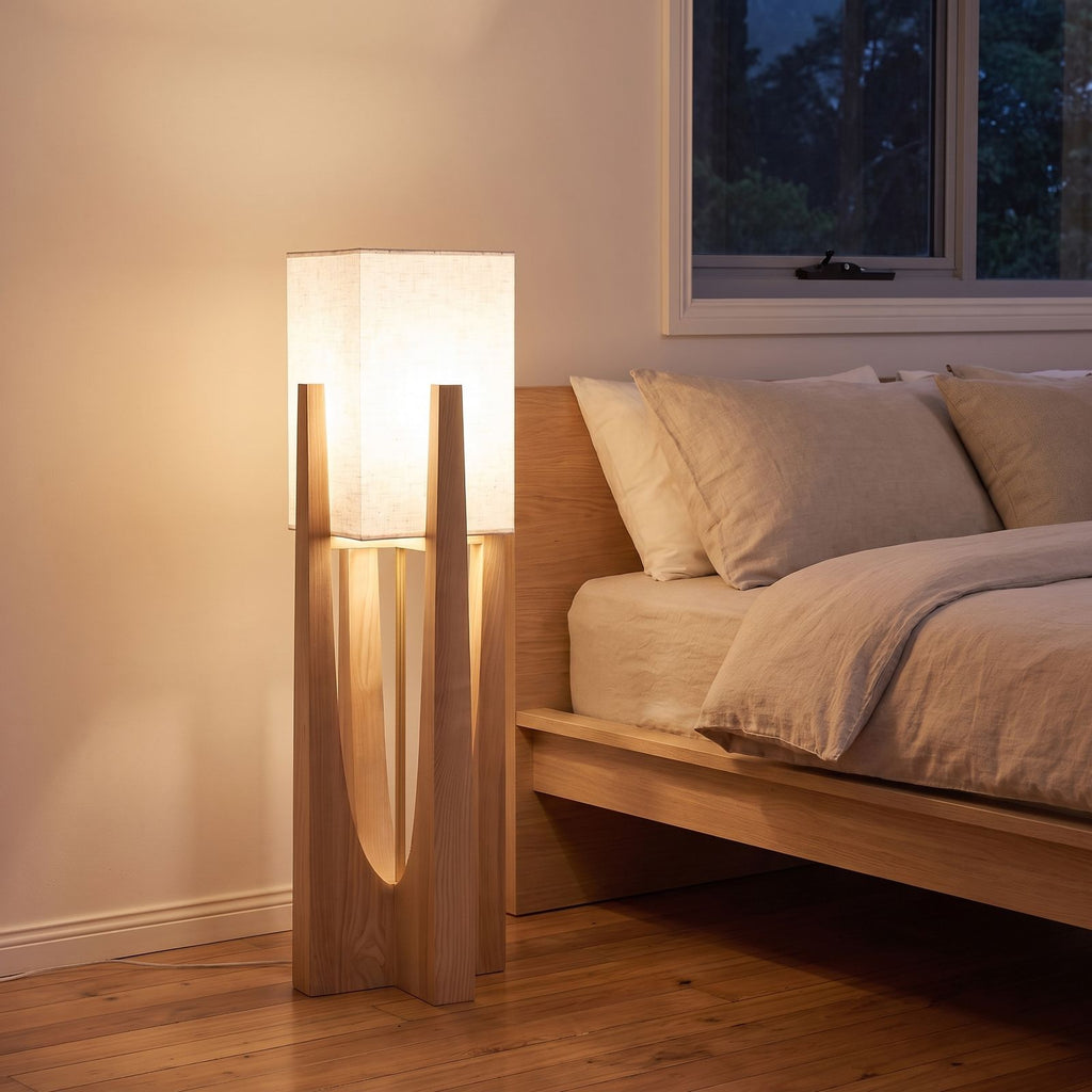 Wood frame fabric shade floor lamp in a bedroom corner beside a low bed