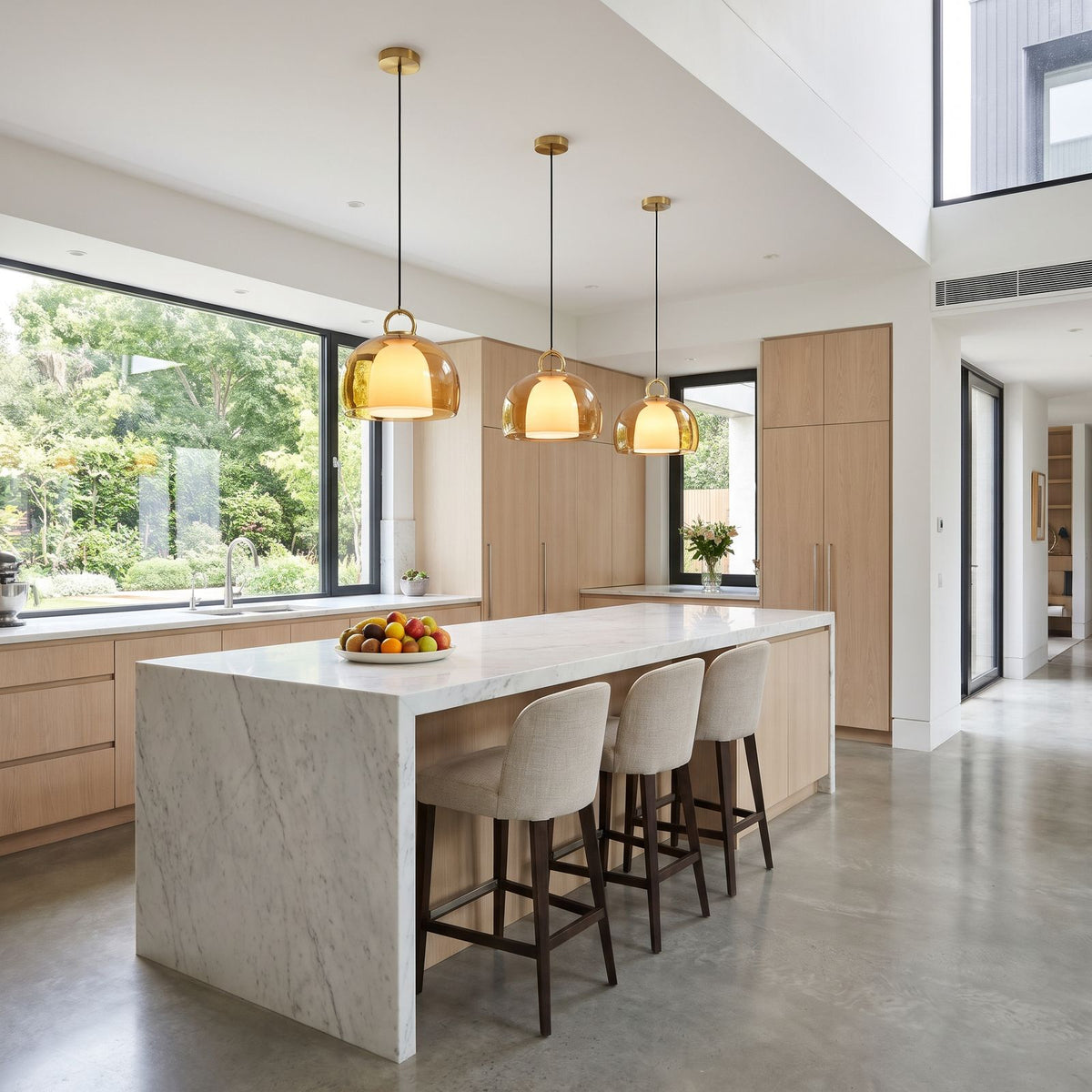 Three of the amber glass dome pendants in a row above a marble kitchen island