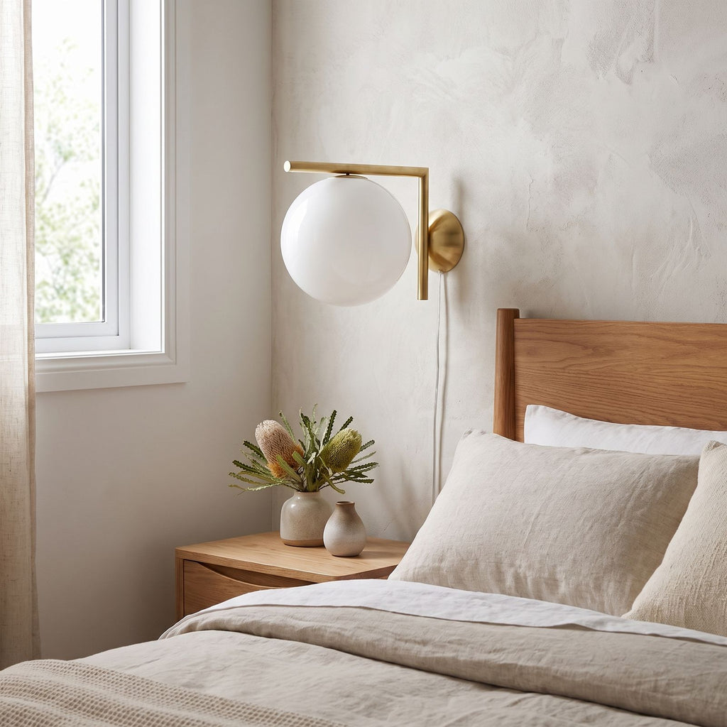 L-Arm Brass and White Glass Globe Wall Light on a bedroom wall beside the bed
