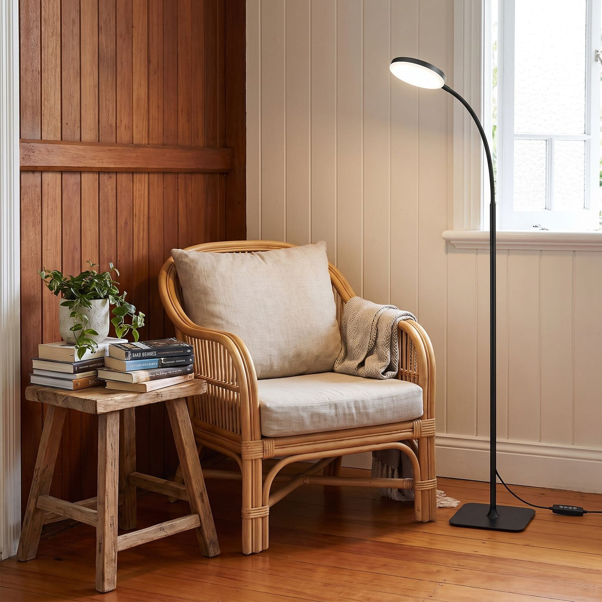 Gooseneck floor lamp beside a rattan armchair in a living room reading nook