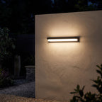 Linear Acrylic Outdoor Wall Light glowing on a garden wall at night