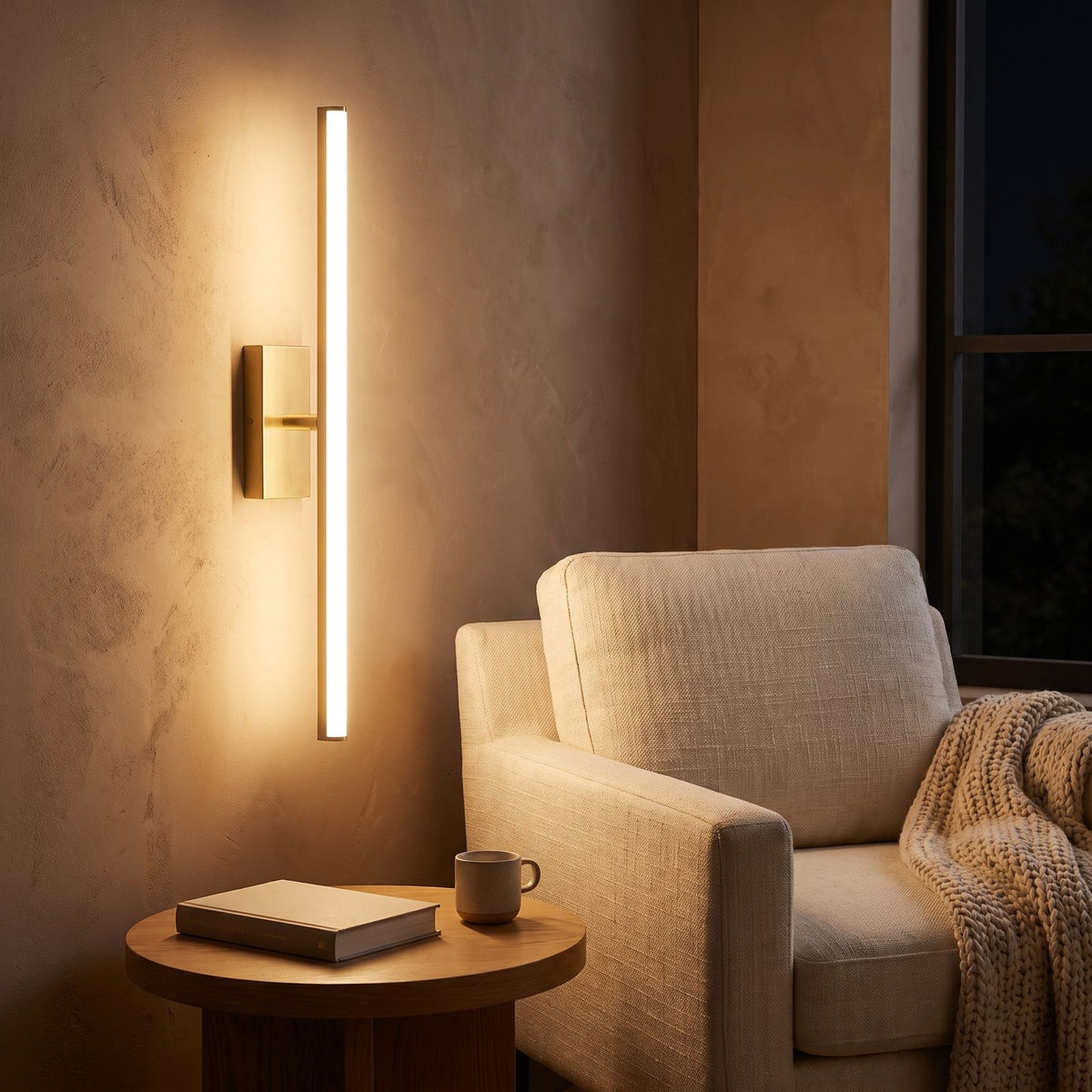 Linear brushed brass LED wall light mounted vertically in a reading corner
