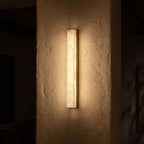 Long Alabaster Bar LED Wall Light glowing on a plaster wall at night