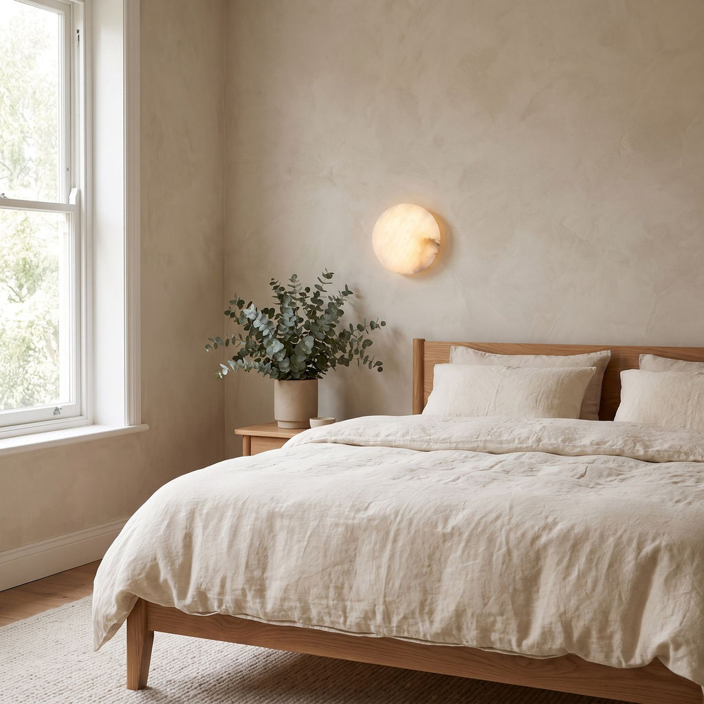 Low-Profile Round Alabaster LED Wall Light on a bedroom wall beside the bed