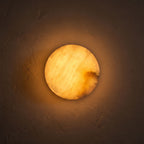 Low-Profile Round Alabaster LED Wall Light glowing on a plaster wall at night