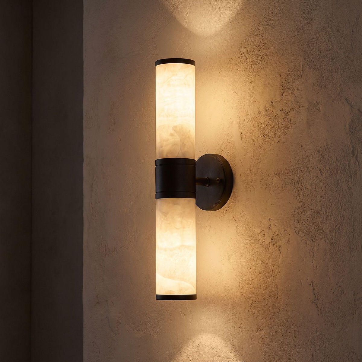 Marble and Cast Iron Up Down Wall Sconce glowing on a plaster wall at night