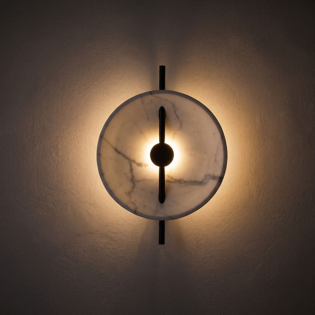 Marble Disc and Black Bar Wall Light glowing on a plaster wall at night