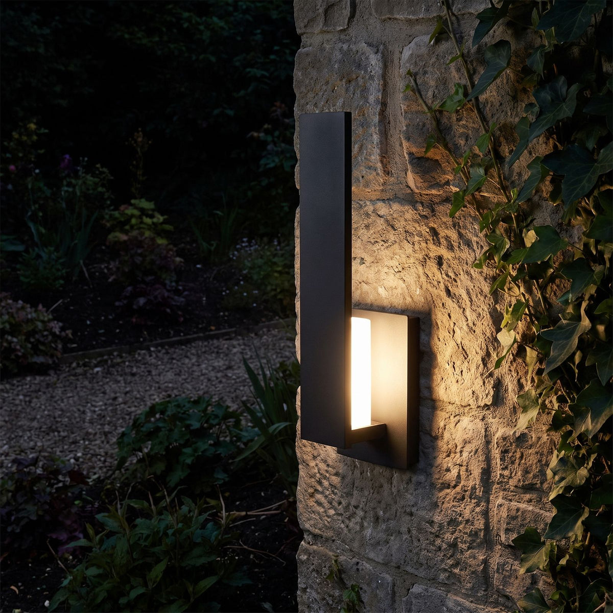 Matte Black Aluminium Lantern Outdoor Wall Light glowing on a garden wall at night