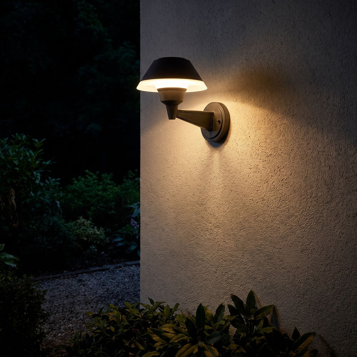 Matte Black Bowl Outdoor Wall Light glowing on a garden wall at night