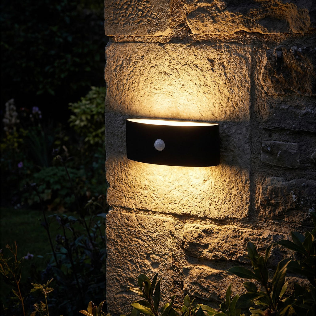 Metal and Acrylic Up Down Outdoor Wall Light glowing on a garden wall at night