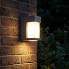 Metal and Glass GU10 Outdoor Wall Light glowing on a garden wall at night