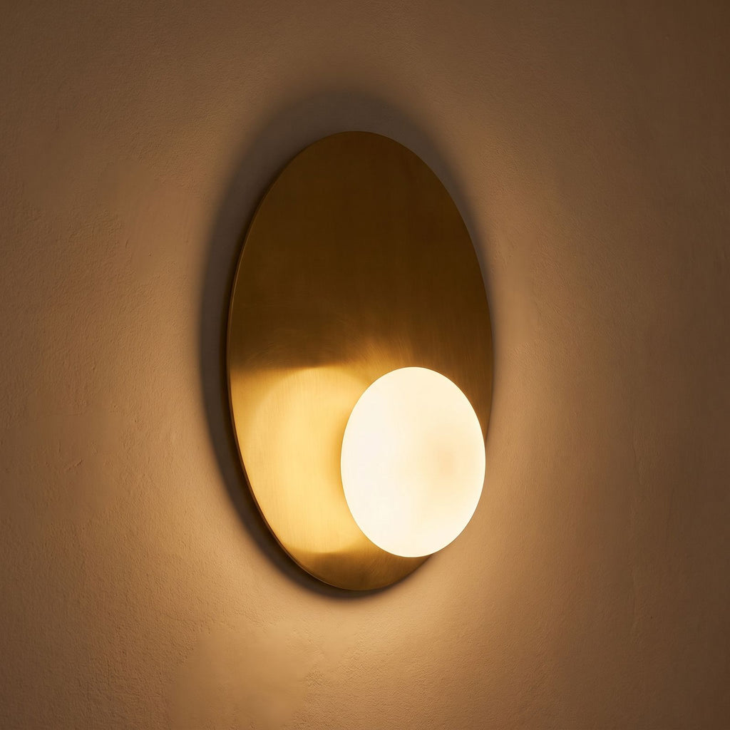 Metal Disc and Opal Glass Wall and Ceiling Light glowing on a plaster wall at night