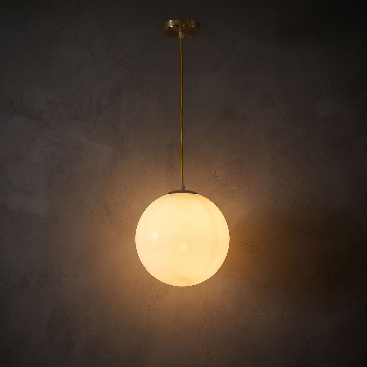 Milky Glass Globe Pendant Light glowing against a plaster wall at night