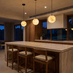 A row of three Mini Alabaster Globe LED Pendant Lights over a stone kitchen island