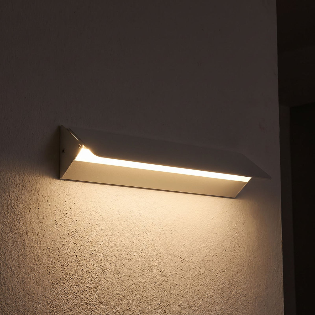 Minimalist White Metal Bar LED Wall Light glowing on a plaster wall at night