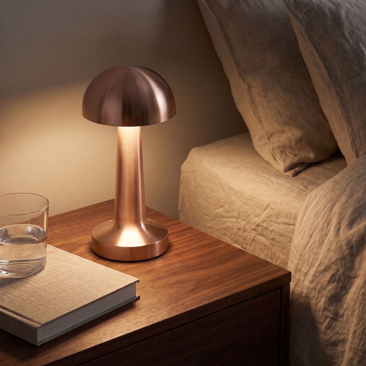 Mushroom Dome Metal Rechargeable Table Lamp in rose gold on a bedside table