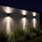 Three black up down outdoor wall lights along a garden wall at night