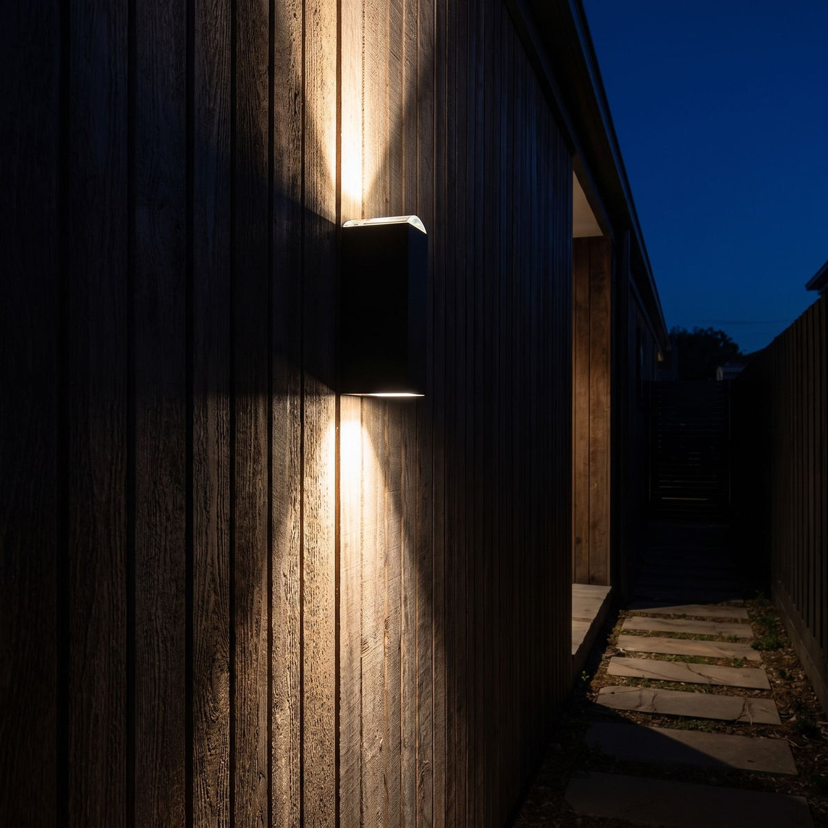 Black up down outdoor wall light on a timber clad side passage at night