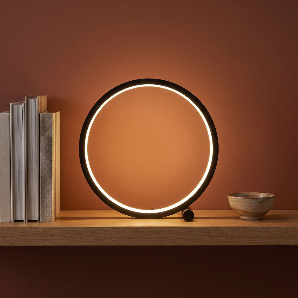 Black open ring table lamp on a shelf beside books