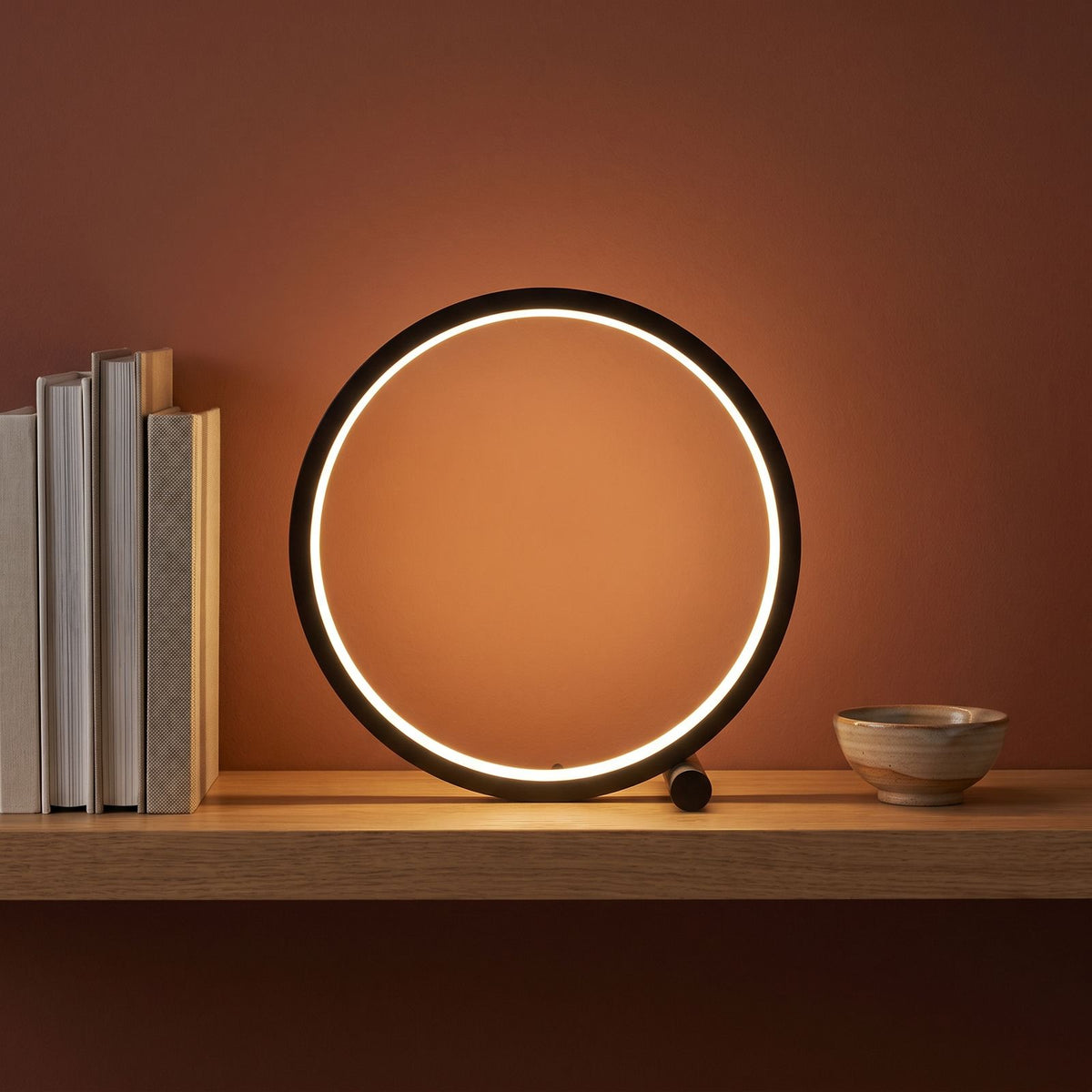 Black open ring table lamp on a shelf beside books
