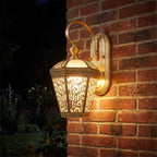 Ornate Brass and Glass Outdoor Wall Light glowing on a garden wall at night