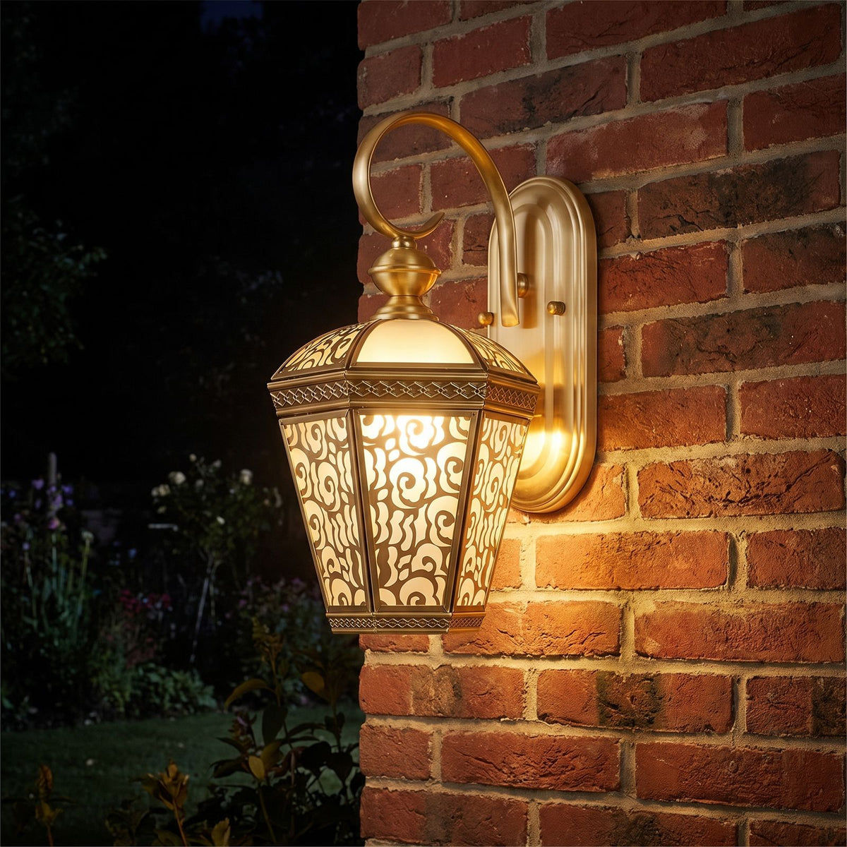 Ornate Brass and Glass Outdoor Wall Light glowing on a garden wall at night