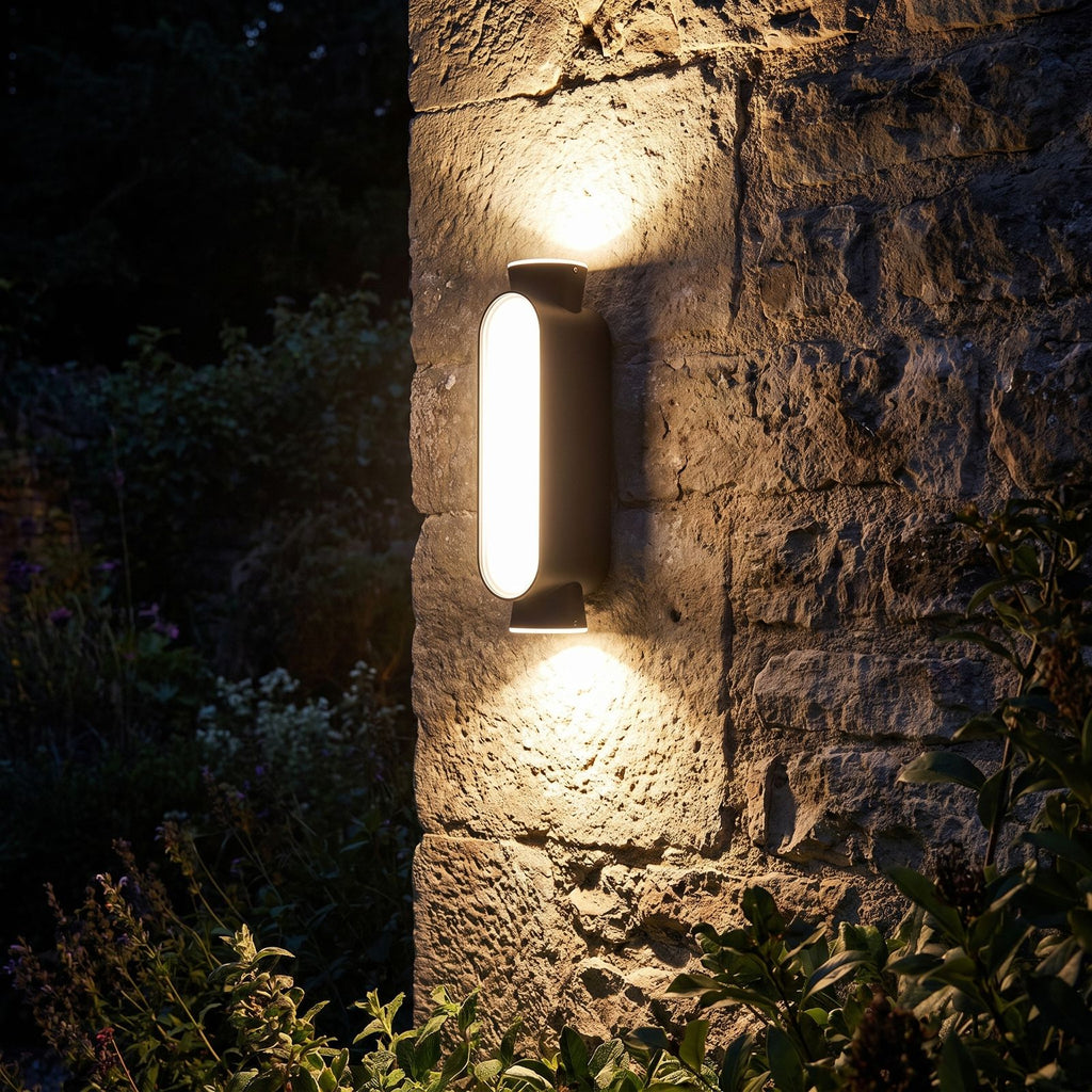 Oval Up Down Acrylic Outdoor Wall Light glowing on a garden wall at night