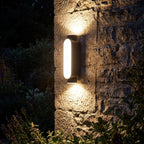 Oval Up Down Acrylic Outdoor Wall Light glowing on a garden wall at night