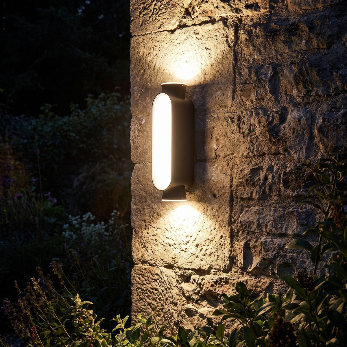 Oval Up Down Acrylic Outdoor Wall Light glowing on a garden wall at night
