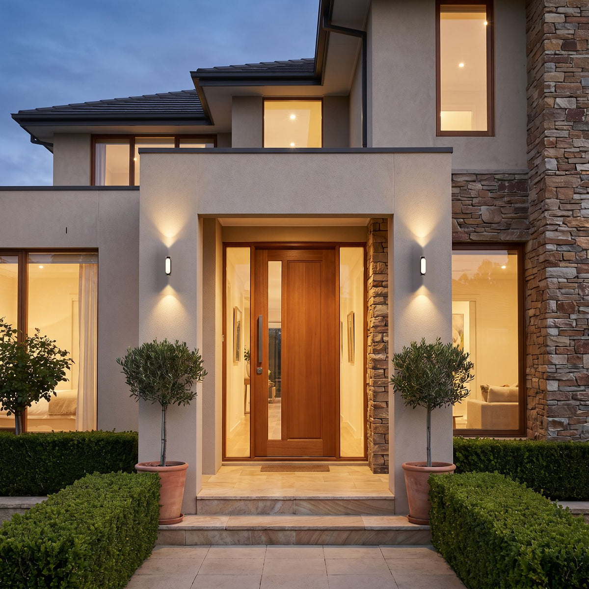 Pair of Oval Up Down Acrylic Outdoor Wall Lights either side of the front door of a stone and render house at dusk
