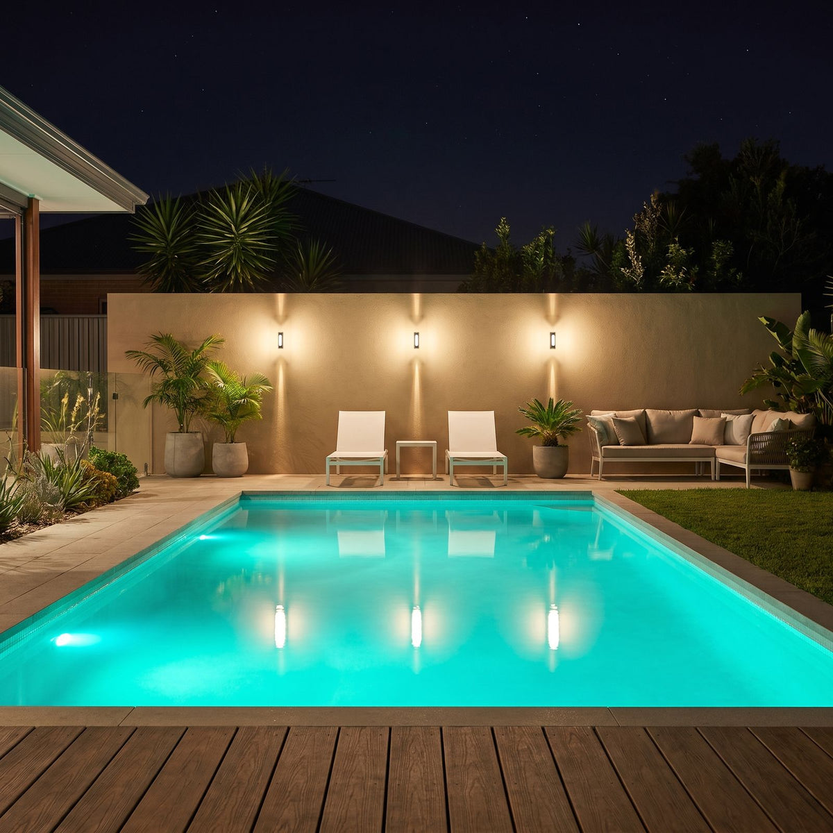 Three Oval Up Down Acrylic Outdoor Wall Lights on a pool feature wall at night beside sun loungers